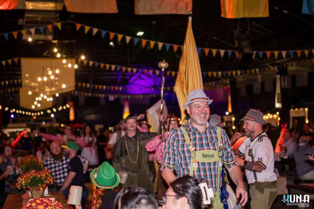 vancouver event photography - A man in a plaid shirt and lederhosen leading a procession through the crowded Harvest Haus festival hall.