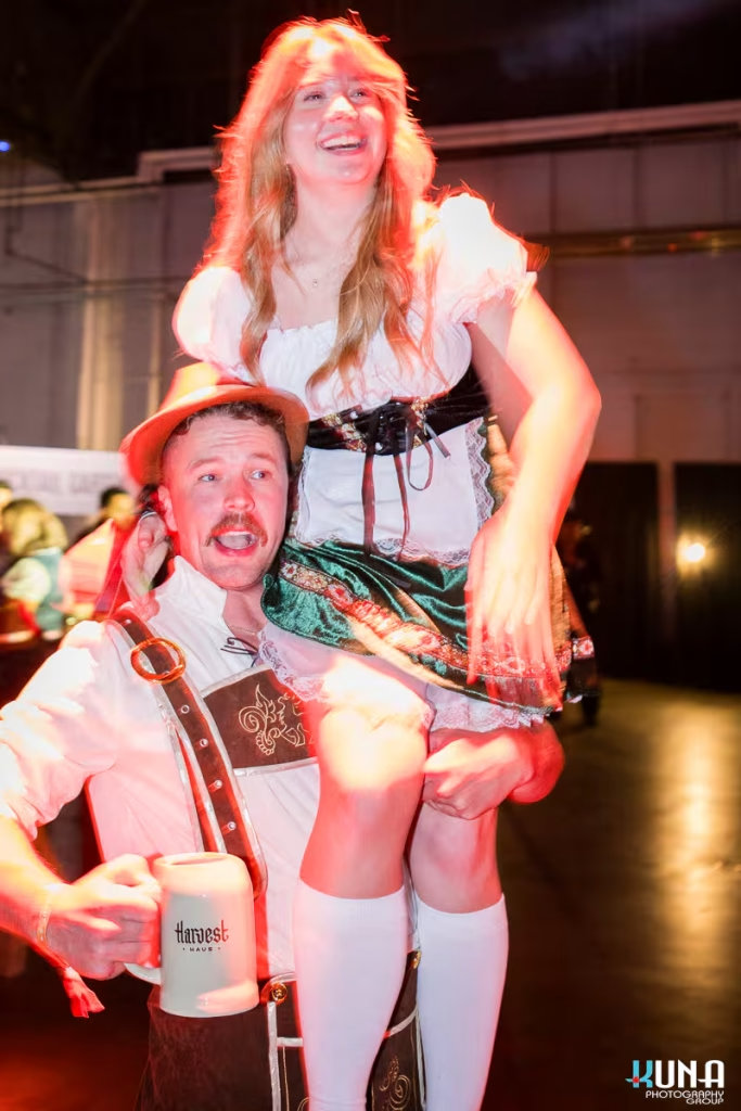 vancouver event photography - A man in lederhosen holding a woman on his shoulders while cheering with a Harvest Haus mug at the Vancouver festival.