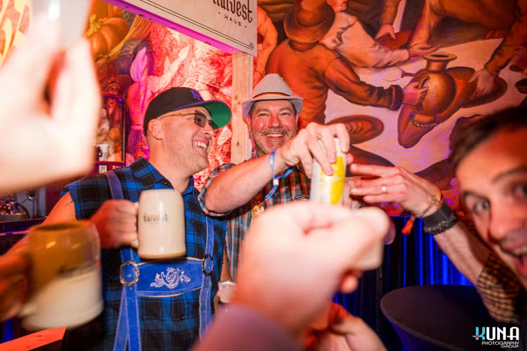 vancouver event photography - Close-up of men, Tyson Villeneuve, in traditional hats and blue plaid shirts laughing and clinking Harvest Haus mugs in a festive beer hall.