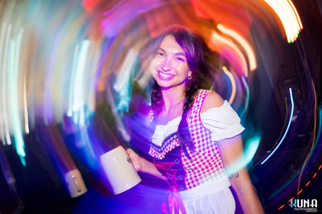 vancouver event photography - Artistic motion-blur shot of a smiling woman in a red-checkered dirndl holding a Harvest Haus beer mug at the festival.
