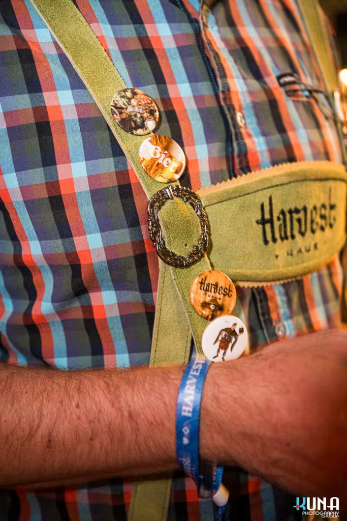 vancouver event photography - Close-up of traditional green lederhosen suspenders with decorative Harvest Haus pins and a blue event wristband.
