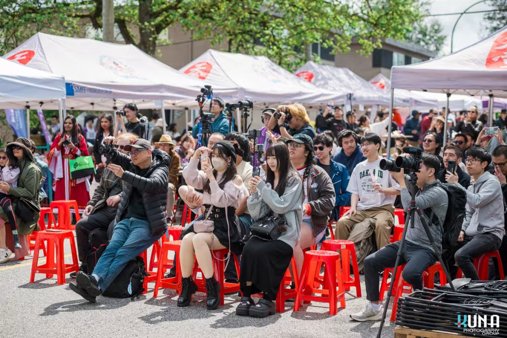 Engaged spectators sitting on iconic red stools taking pictures with their phones during TJ Fest event photography in Burnaby.