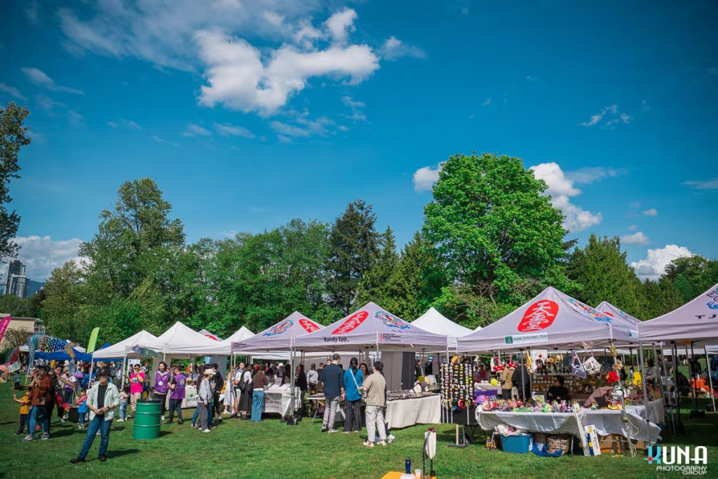 TJ Fest 2025 Kuna Photography: Vancouver Event Photographer. Wide shot of vendor tents and crowds under a blue sky at TJ Fest in a Burnaby park, BC.