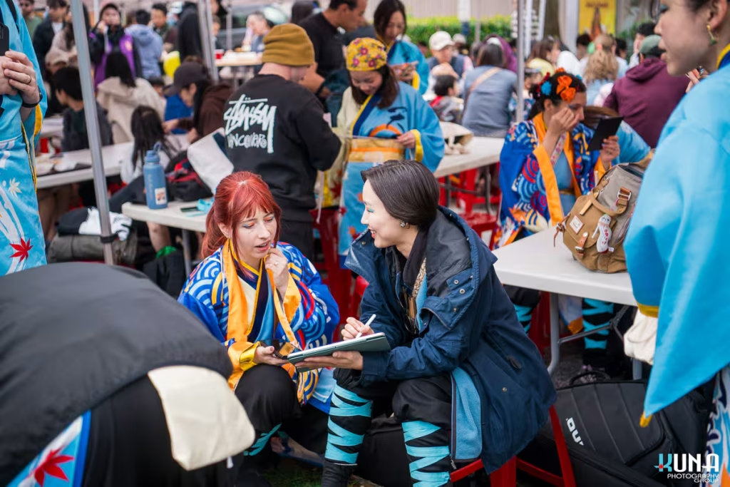 TJ Fest 2025 Kuna Photography: Vancouver Event Photographer. Performers in traditional blue costumes resting & chatting on a tablet at a festival in Vancouver, BC.
