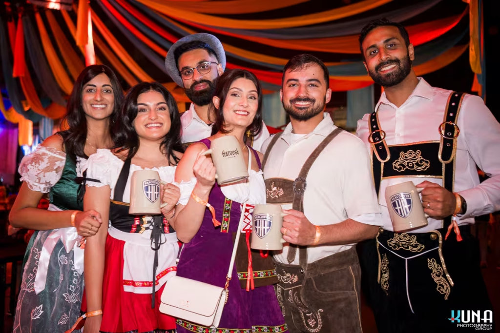 vancouver event photography - Portrait of five smiling attendees in traditional German outfits holding branded Harvest Haus beer steins.