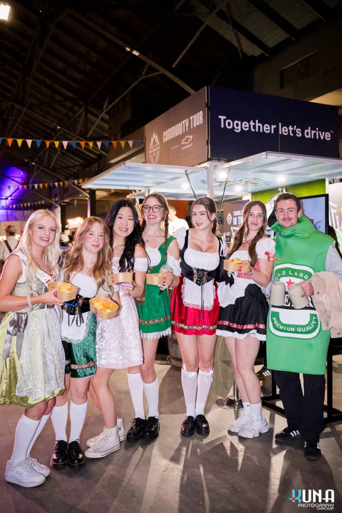 vancouver event photography - A group of friends in traditional dirndls and a beer bottle costume posing with steins and snacks at Harvest Haus Vancouver.