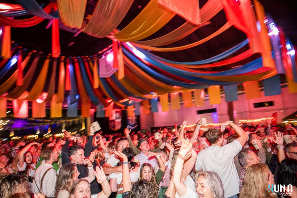 vancouver event photography - Wide shot of a massive crowd dancing with their hands up under colorful ceiling drapes at Harvest Haus Vancouver.