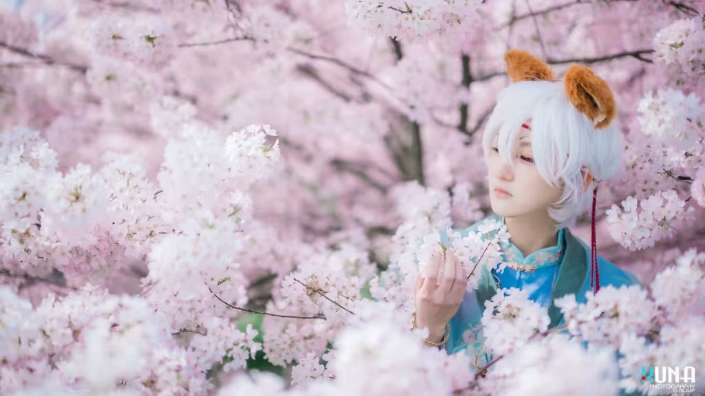 Close-up portrait of white-haired fox boy cosplayer among pink cherry blossoms in Vancouver.