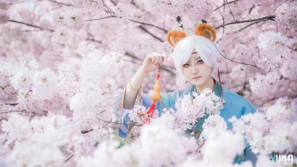 Fox boy cosplayer with white hair and orange ears posing with a gourd in cherry blossoms.