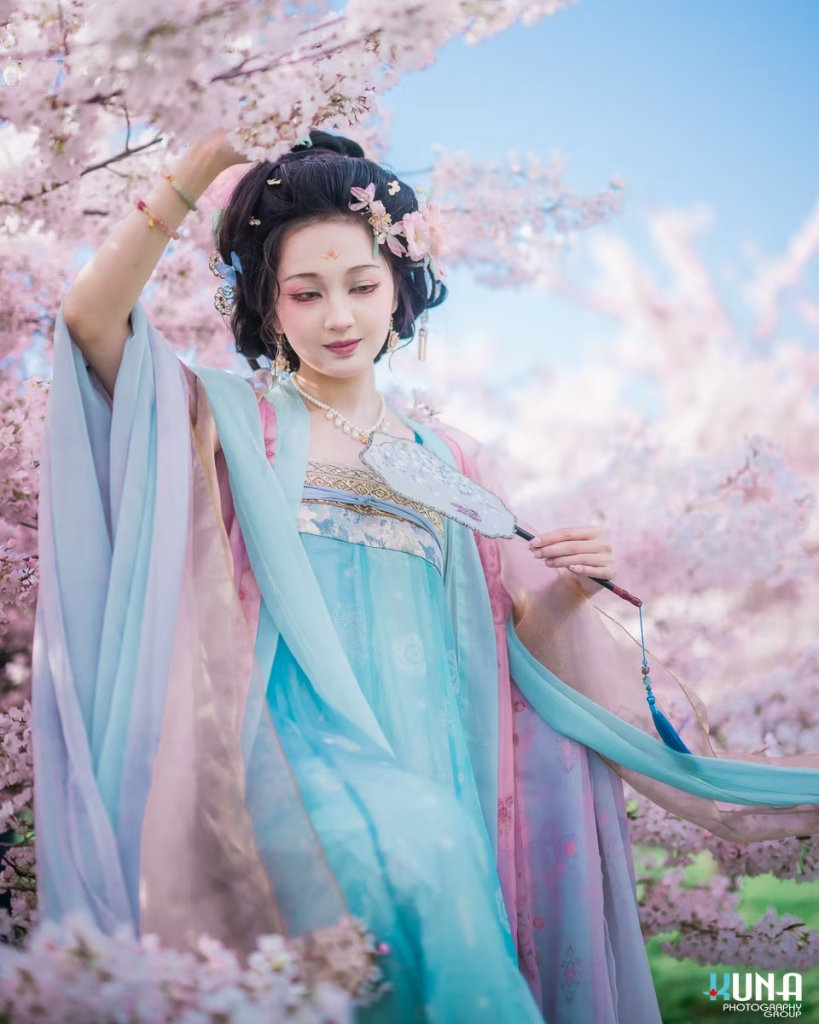 Hanfu portrait of a woman holding a traditional fan under cherry trees.