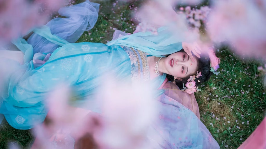 Vancouver HanFu Portrait - Woman in traditional blue and pink Hanfu lying on the grass surrounded by spring cherry blossoms in Vancouver.