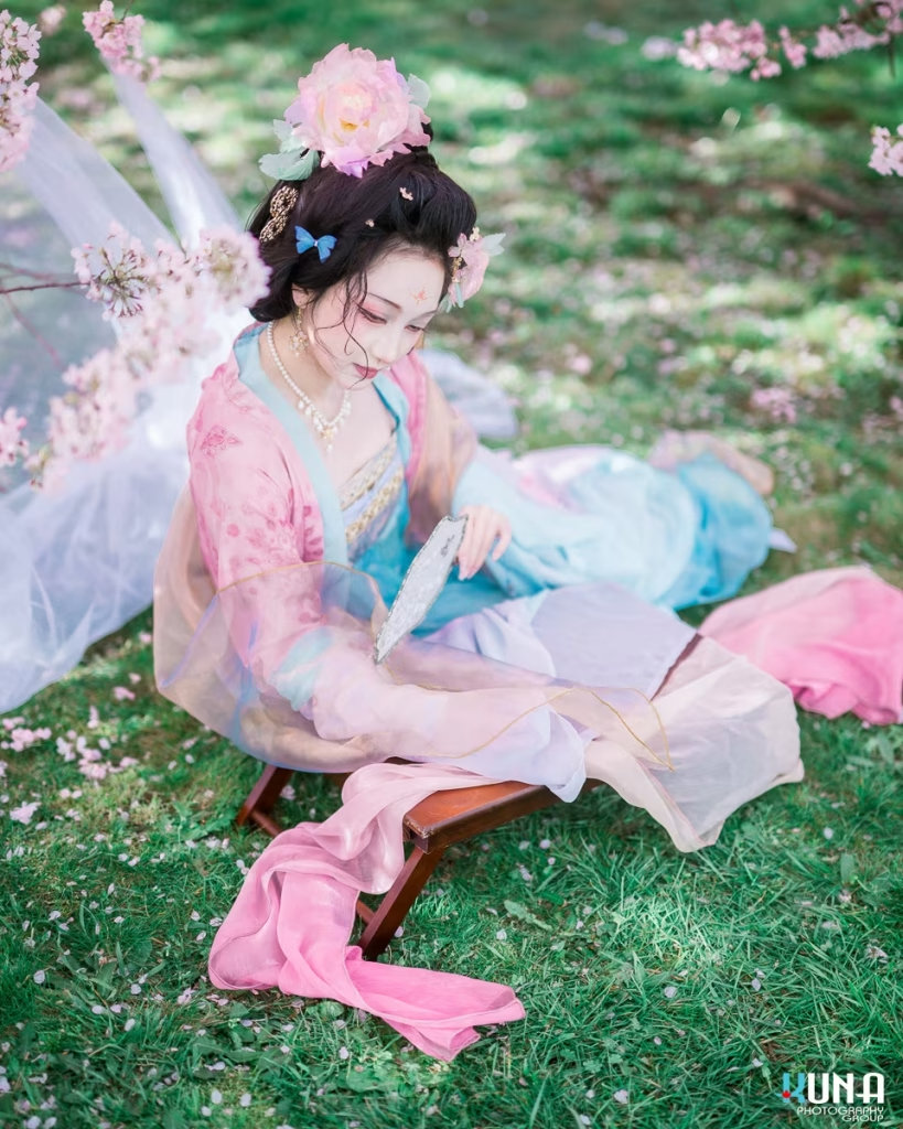 Lady in Hanfu sitting gracefully on green grass with a fan in Vancouver.
