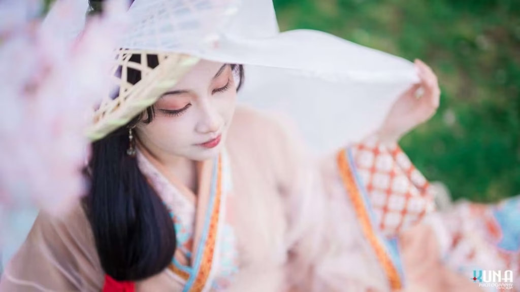 Elevated angle hanfu portrait in Metro Vancouver: Subject looking down through a veiled bamboo hat among cherry blooms at Larry Berg Flight Path Park 2025.