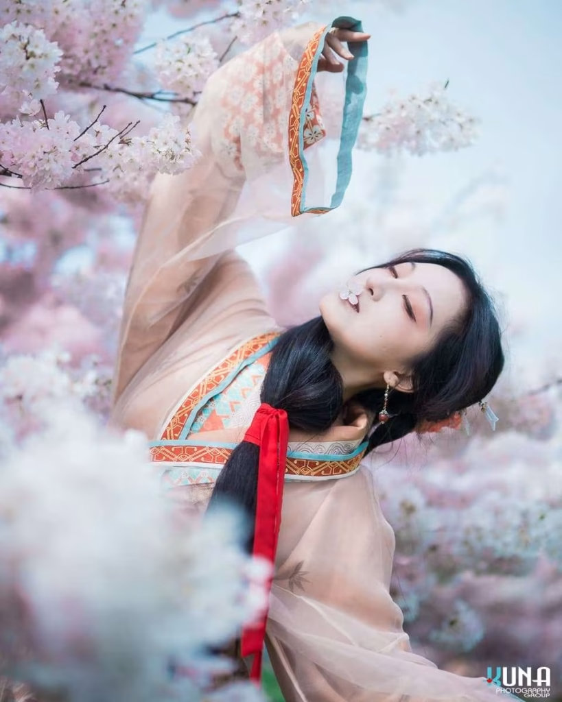 Dynamic hanfu photography in Metro Vancouver: A flowing pose with a petal on lips under cherry trees at Larry Berg Flight Path Park BC 2025.