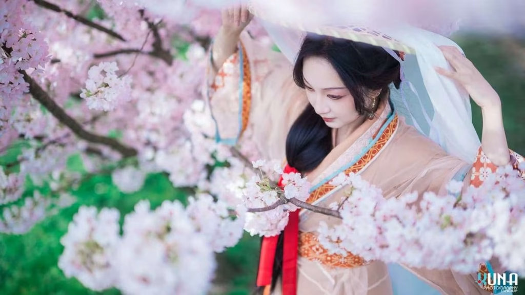 Atmospheric hanfu portrait detail in Richmond: Model surrounded by heavy bokeh of cherry blossoms lifting a veil at Larry Berg Flight Path Park Vancouver.
