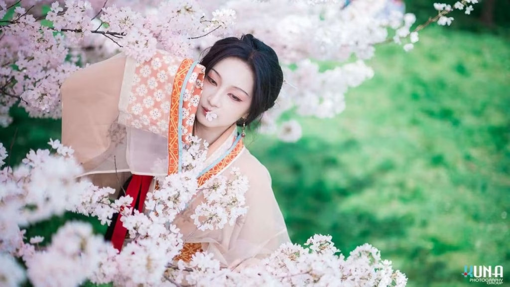 Playful hanfu portrait among dense cherry blossoms in Richmond: Subject looking at camera with sleeve raised at Larry Berg Flight Path Park Vancouver 2025.