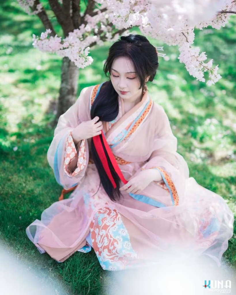 Traditional hanfu portrait profile in Richmond: Subject looking down adjusting hair among cherry blooms at Larry Berg Flight Path Park Vancouver BC.