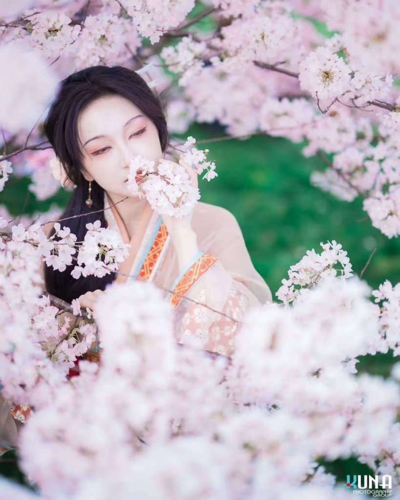 Atmospheric hanfu portrait detail in Richmond: Model surrounded by heavy bokeh of cherry blossoms smelling the flowers at Larry Berg Flight Path Park Vancouver.