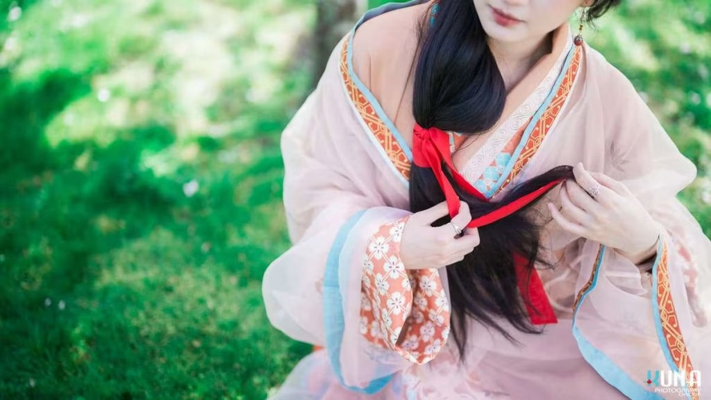 Hanfu dress detail in Metro Vancouver: Close-up of layered fabrics, gold trim, and tying a red hair ribbon at Larry Berg Flight Path Park 2025.