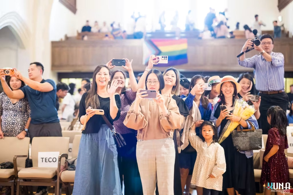 Smiling audience members standing up and taking photos with their smartphones at a community concert