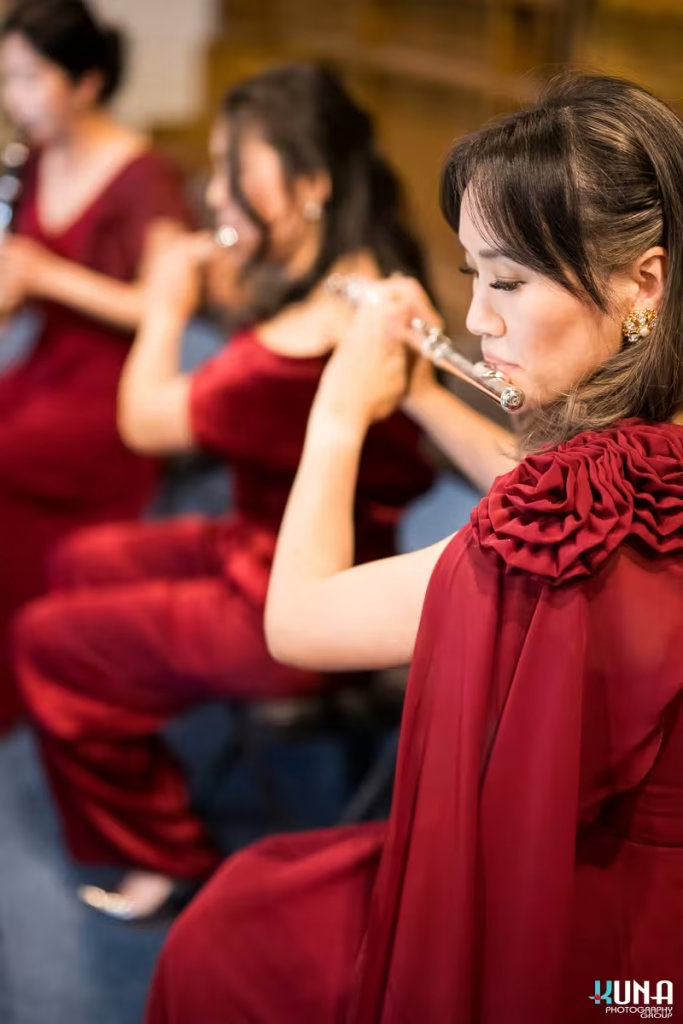 Close up portrait of a female flutist in a red gown with rose details playing classical flute