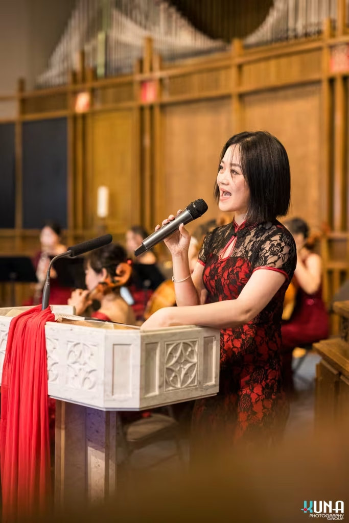 emale master of ceremonies speaking into a microphone at the podium wearing a lace cheongsam dress