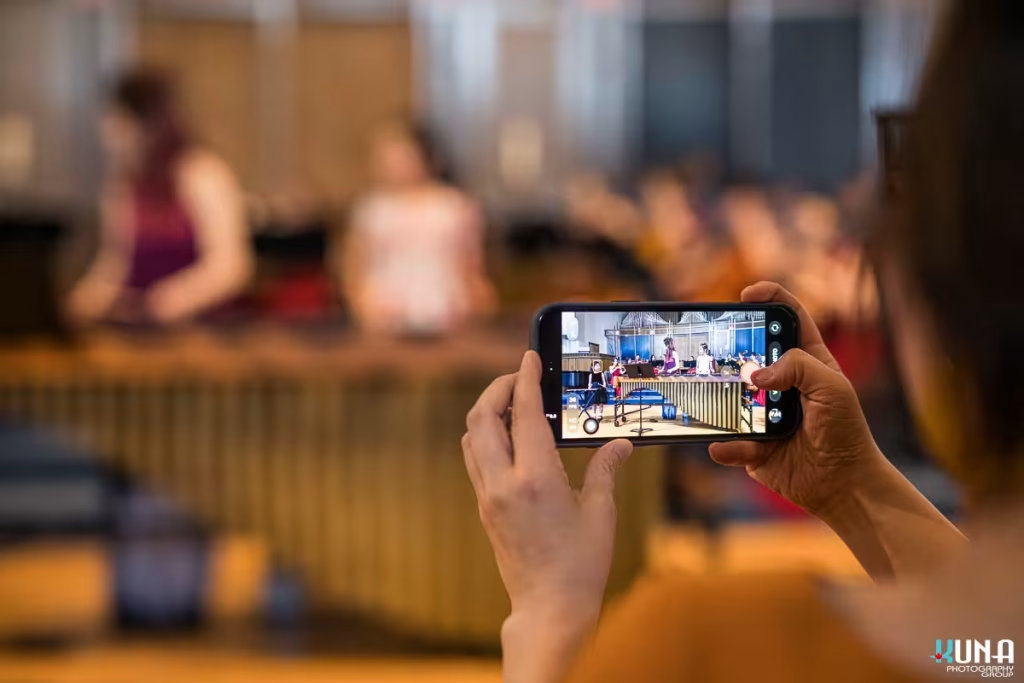 An audience member using a smartphone to record a live marimba performance on stage