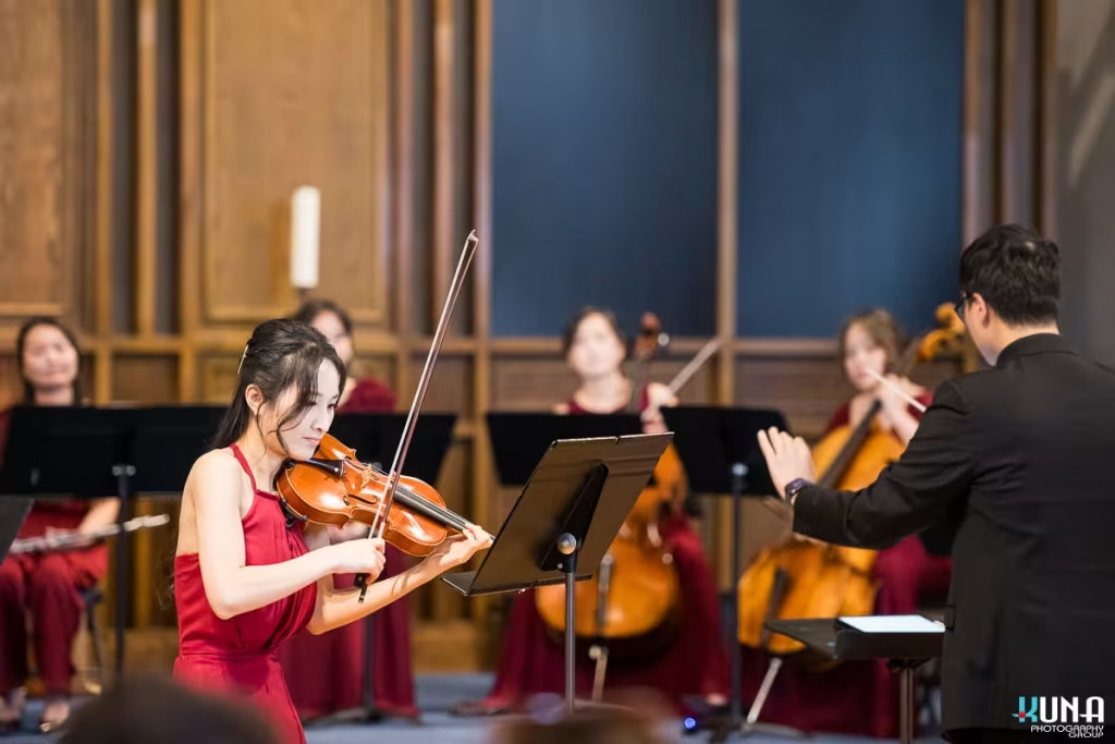 Female violin soloist playing intensely with the orchestra and conductor in the background