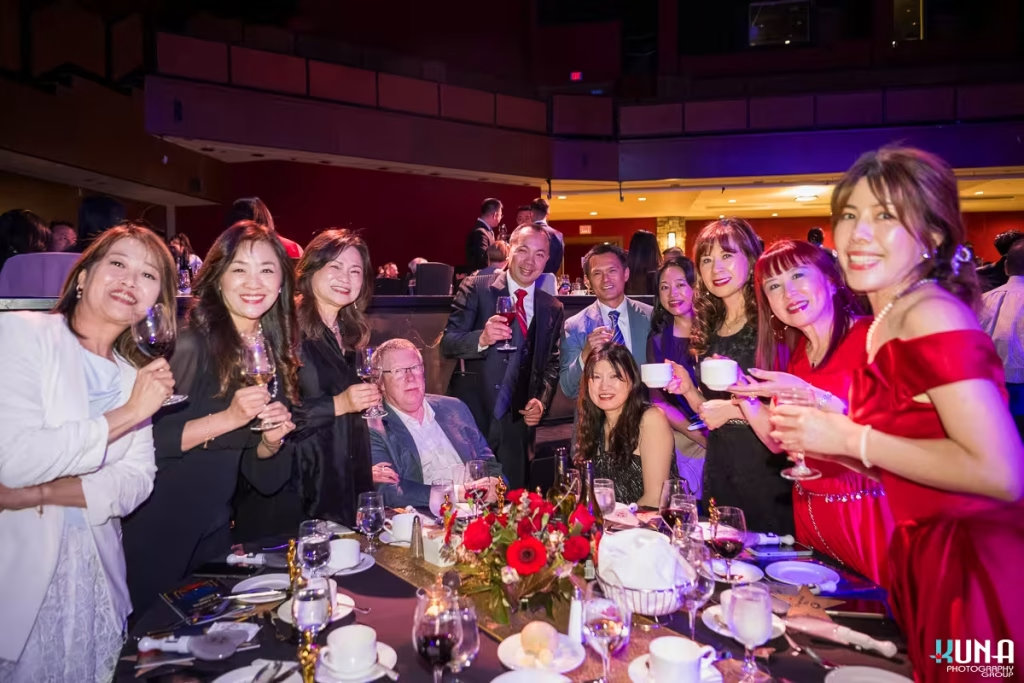 Guest table toast photography by Vancouver gala photographer Guests smiling and raising wine glasses for a toast around a formal dinner table.