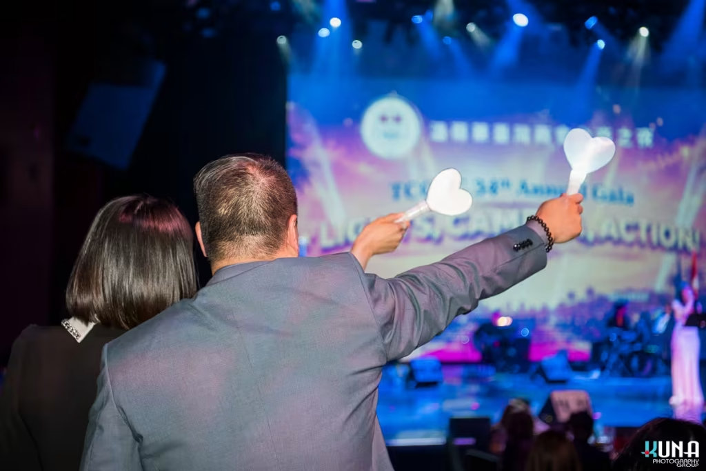 Immersive audience interaction photography at River Rock Theatre Behind the back view of guests waving glowing white heart light sticks toward the stage.