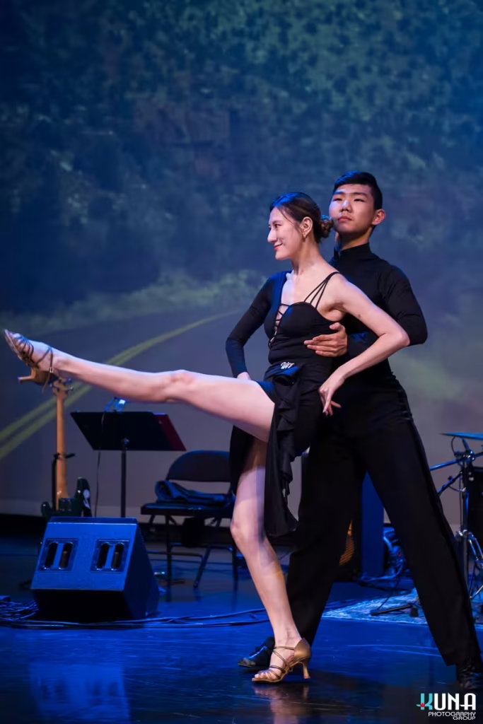 Professional ballroom dance stage photography at corporate gala A dancing couple performing a striking ballroom routine with a leg extension on stage.