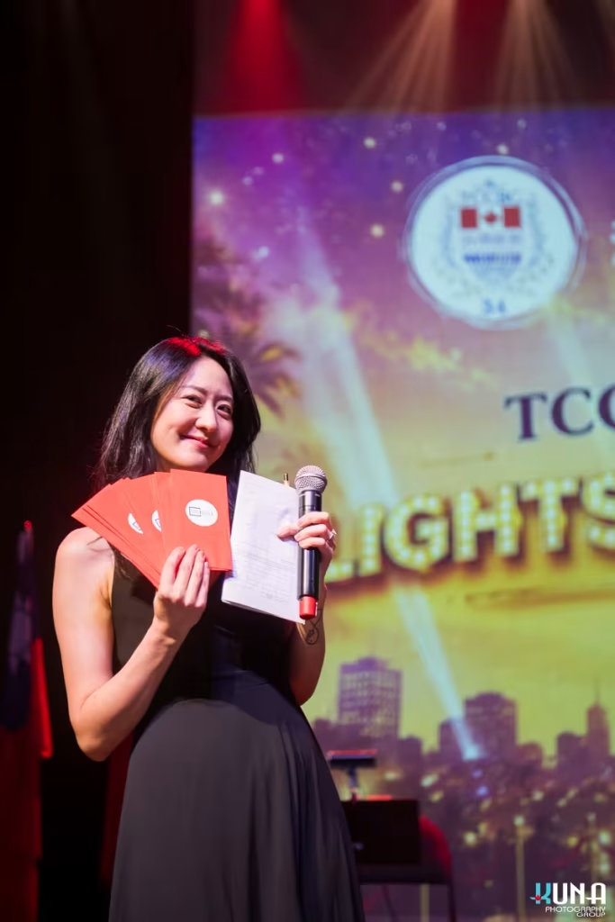 Lucky draw segment host photography by Vancouver gala photographer Smiling host, Jessica, on stage holding a microphone and several red envelopes.