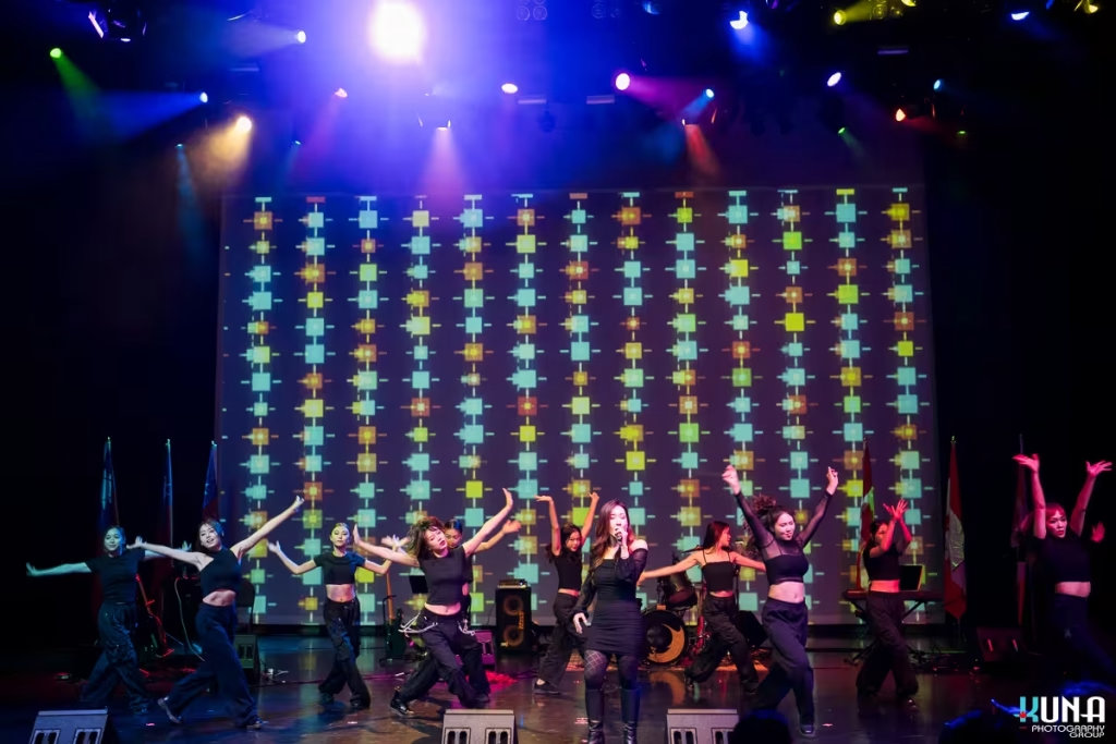 Grand musical production stage coverage by Vancouver gala photographer Full stage dance troupe performing an energetic routine under bright multi coloured spotlight beams.