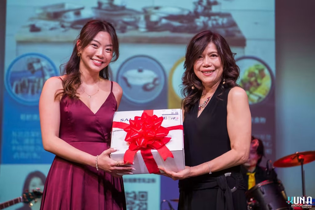 Corporate prize winner presentation by Vancouver gala photographer Two ladies smiling proudly while displaying a beautifully wrapped white gift box with a red bow on stage.