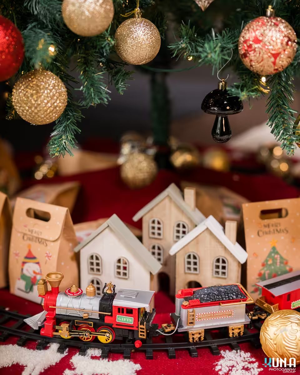 A festive toy train passing miniature wooden houses under the tree at our Vancouver Christmas Mini Sessions.